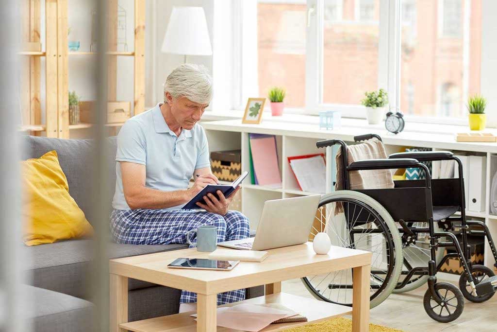 A disabled elderly person in a wheelchair sitting on the sofa at home