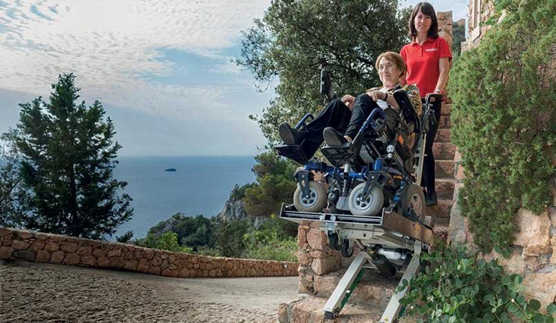 Une dame handicapée est transportée dans l'escalier de pierre à l'aide d'un monte-escalier électrique.