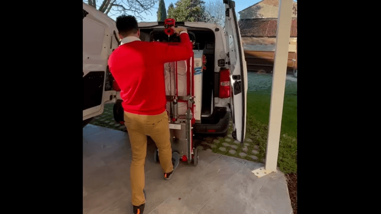 A man loads a washing machine into the van with the electric load lifting function of the stairs dolly