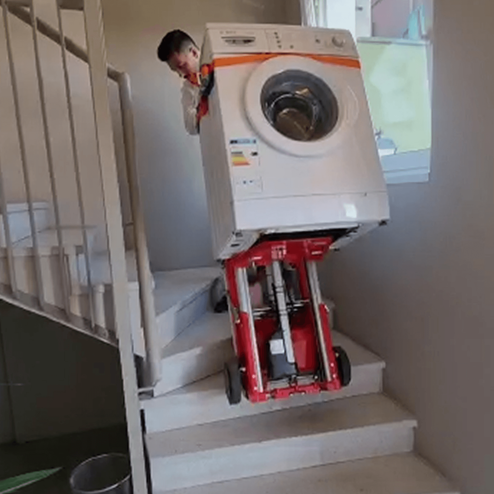 A man transporting a washing machine up stairs with a powered stair climbing dolly 